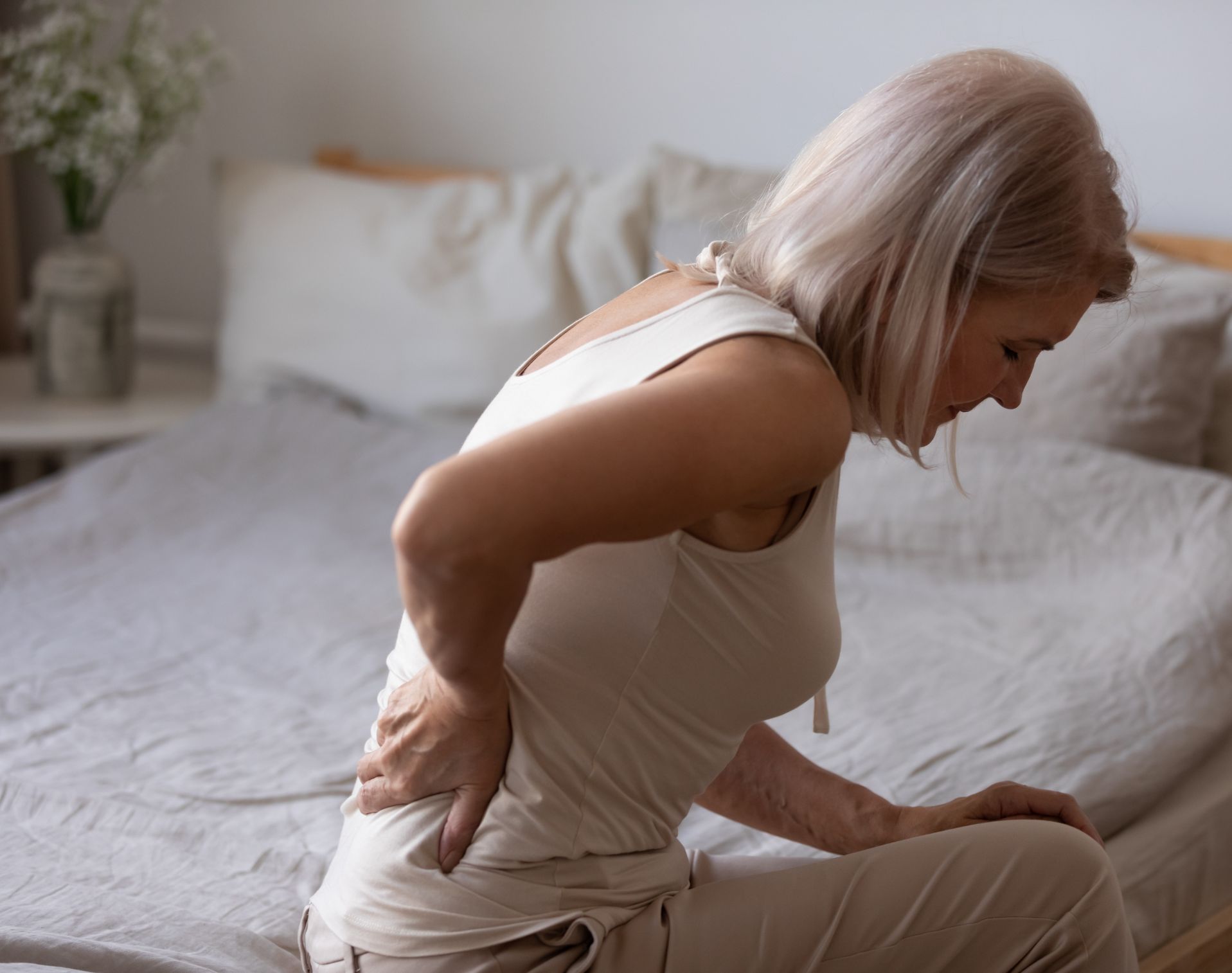 Women sitting on bed with back pain from osteoporosis